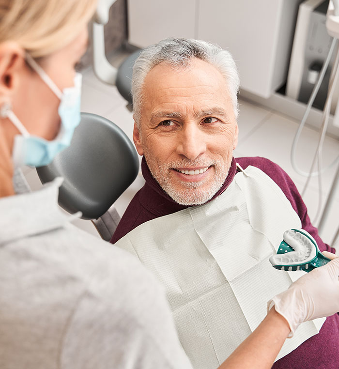 senior man smiling at dentist holding a dental impression for dentures 