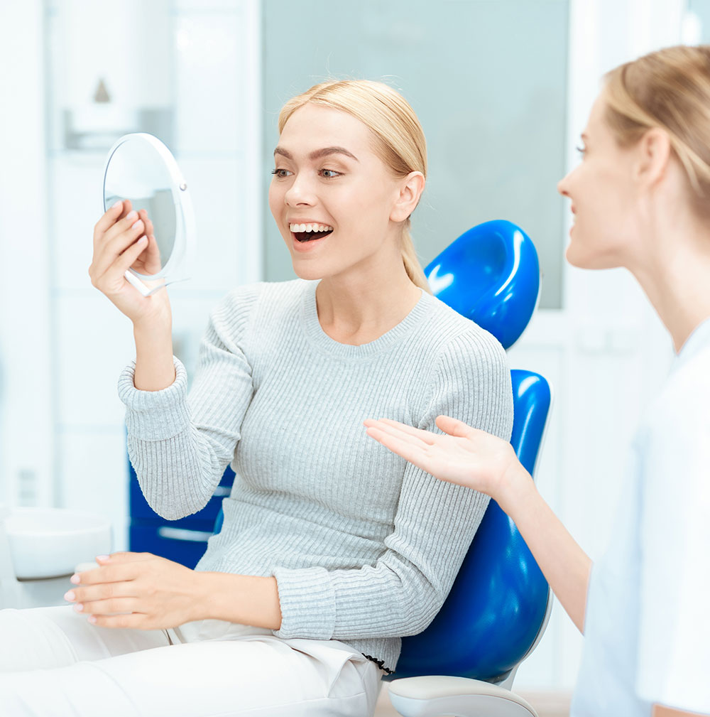 young woman smiling into mirror after receiving teeth whitening treatment at the dentist