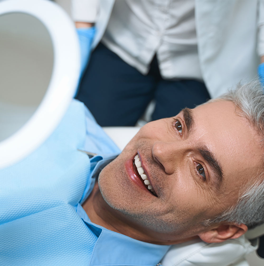 man smiling at mirror image after receiving dental bonding treatment